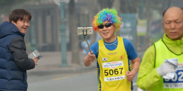 ▲ <“내 패션 어때요”> 익살스러운 가발을 쓴 한 참가자가 달리며 셀카를 찍고 있다.