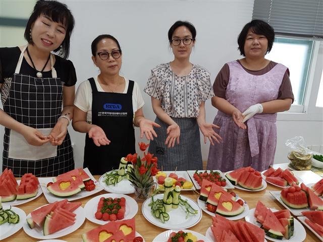 ▲ 전북문화관광재단이 운영하는 ‘문화파출소 덕진’에서 하고 있는 여름특집 과일카빙 수업 수강생들이 자신의 작품 앞에서 기념사진을 찍고 있다.