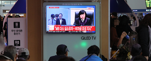 5일 오후 서울역에서 시민들이 이명박 전 대통령의 선고공판 생중계를 보고 있다.    '다스'의 자금을 횡령하고 삼성 등에서 거액의 뇌물을 챙긴 혐의로 기소된 이명박 전 대통령은 이날 재판에 출석하지 않았다. /연합뉴스