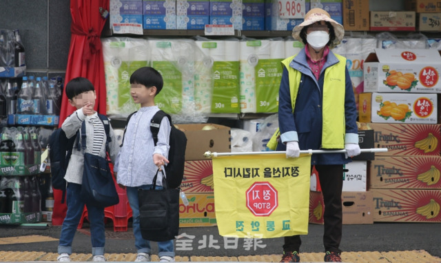 23일 전주 홍산초등학교 앞에서 녹색어머니연합회 회원이 노란 깃발을 들고 아이들의 안전한 등굣길을 도와주고 있다. 조현욱 기자