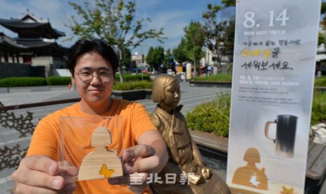 제2회 위안부 기림의 날인 14일 전주시 풍남문광장에서 사용하지 않는 텀블러와 나무소녀상 교환해주는 행사가 열린 가운데 한 시민이 평화의 소녀상 옆에 앉아서 교환한 나무소녀상을 보여주고 있다. 박형민 기자