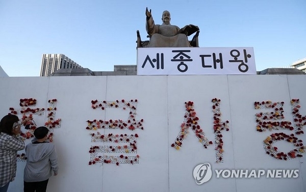 573돌 한글날을 하루 앞둔 8일 오후 서울 세종대로 광화문광장 세종대왕상 앞에서 시민들이 '한글 사랑해'라는 문구가 적힌 나무 판자에 장미꽃을 달고 있다. 연합뉴스