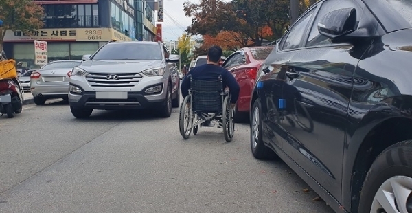 불법주정차로 휠체어 통행이 어려운 가운데 마주 오는 차량을 휠체어를 탄 기자가 위태롭게 피하고 있다.