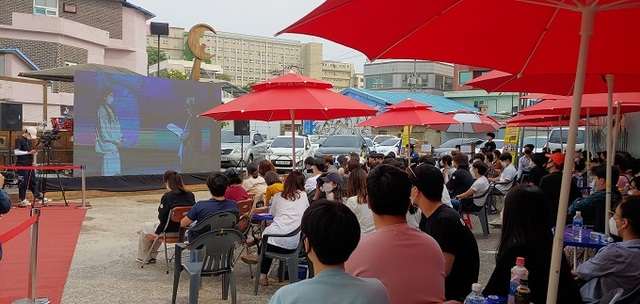 지난 30일 군산시민예술촌에서 ‘제1회 군산개복단편영화제’가 열린 가운데, 시민과 관광객들이 예술촌 야외마당에 마련된 스크린 속 대상 시상 장면을 보고 있다. 같은 시간, 예술촌 공연장에서는 박양기 군산시민예술촌장이 시상자로 나서 대상 수상자 이아주 씨에게 상패를 전달했다.
