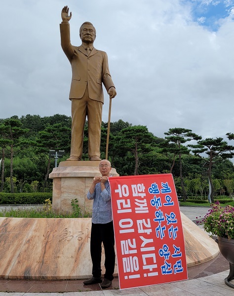 서주원 작가가 전남 무안군 김대중 대통령 동상 앞에서 삭발을 하고 서 있다.